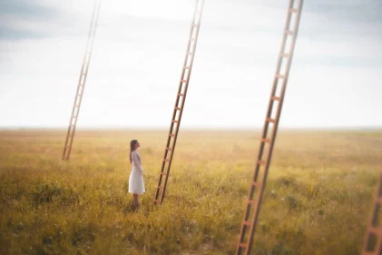 Surreal dreamlike vision of several ladders leading into the sky with lady looking up.